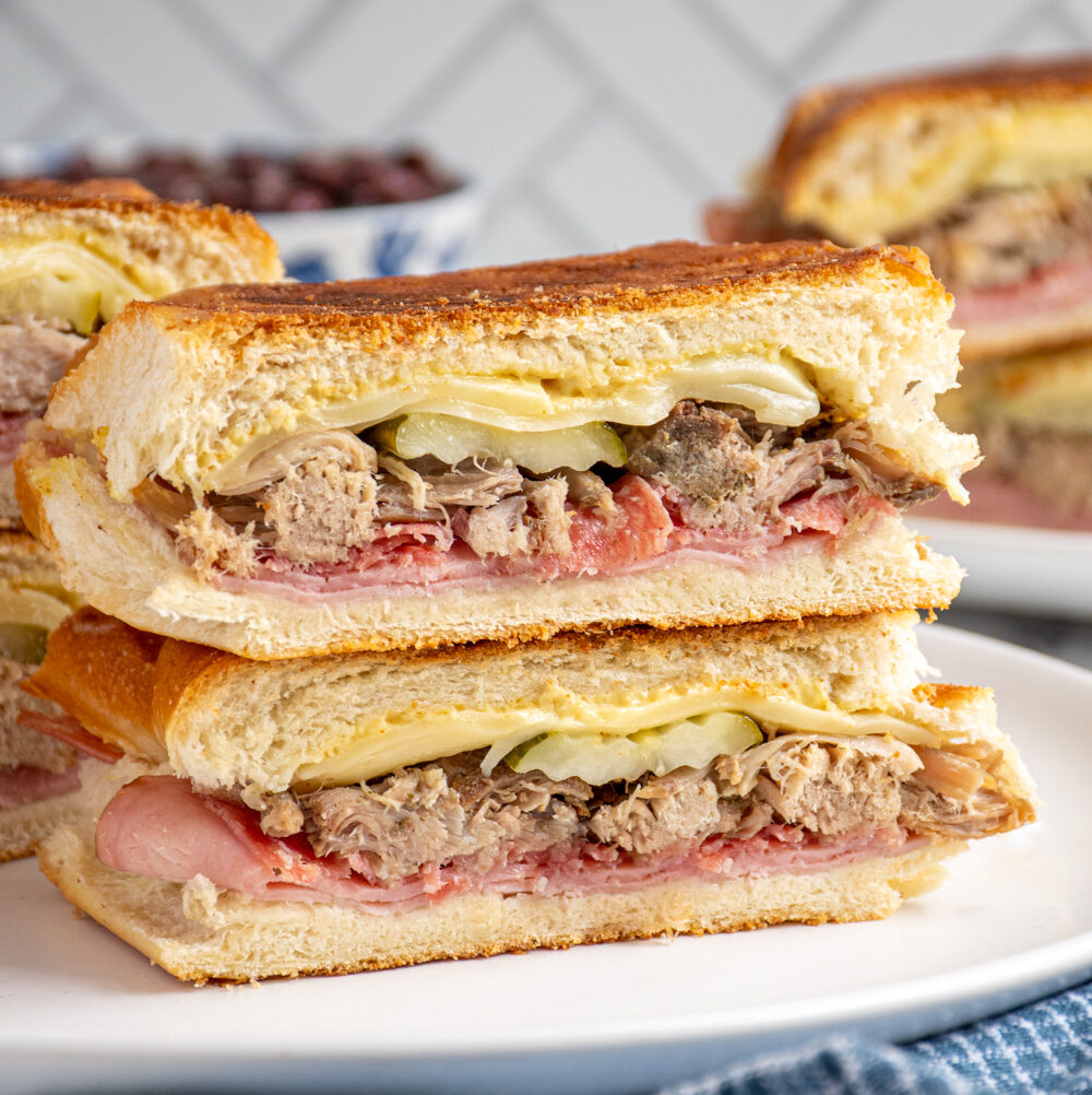 A Cuban sandwich sliced in half and stacked on top of one another showing the ingredients on the inside.