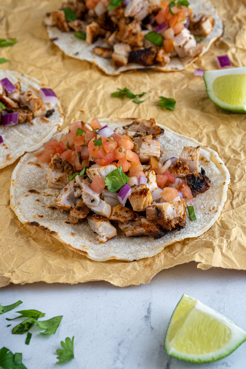 A grilled chicken street taco laid out on a table top filled with chicken and topped with salsa, onions, and cilantro.
