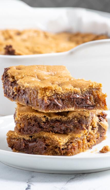 A stack of 3 whole wheat chocolate chip cookie bars on a white plate showing off melty chocolate.
