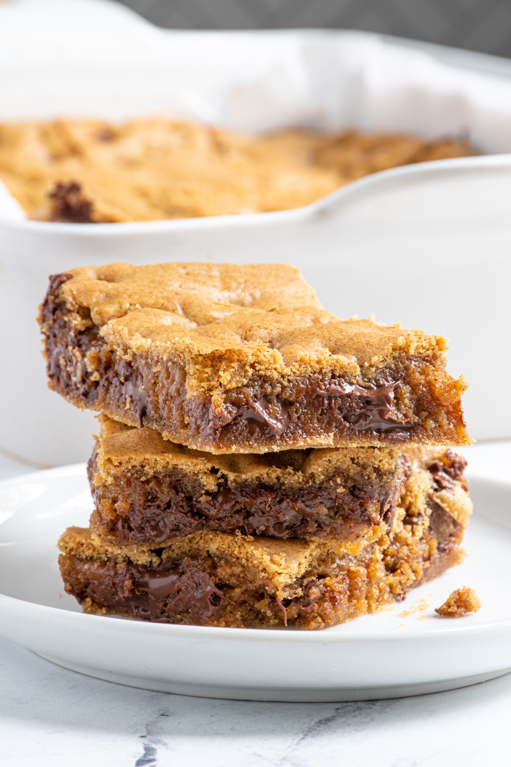 A stack of 3 whole wheat chocolate chip cookie bars on a white plate showing off melty chocolate.