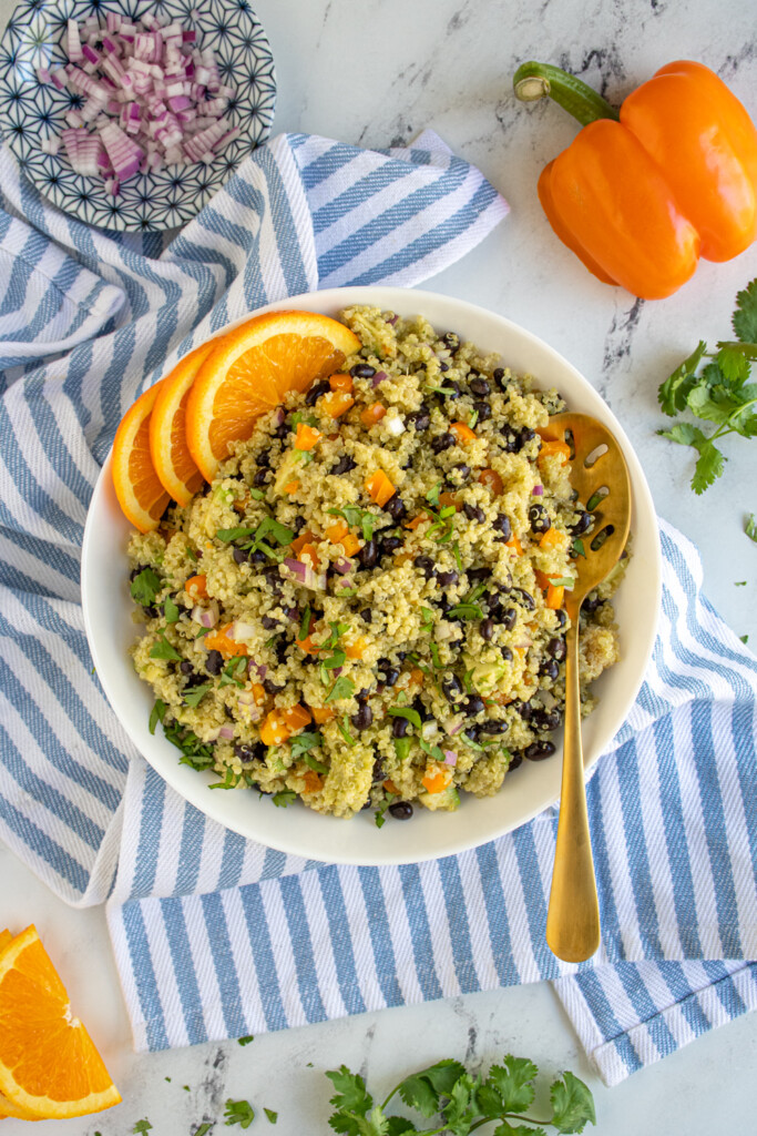 Overhead view of a bowl with a kitchen towel, filled with black bean quinoa salad and topped with orange cilantro dressing.