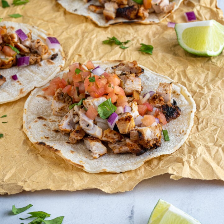 Three grilled chicken street tacos laid out on a table with garnished like lime and cilantro.