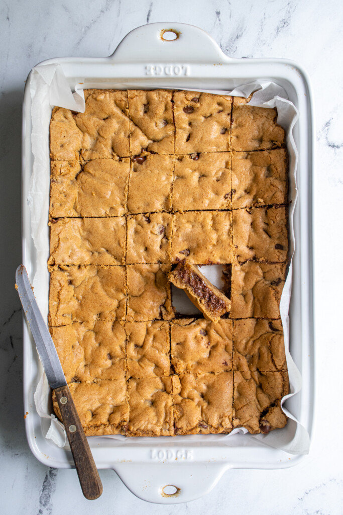 Overhead view of a while baking dish with cut whole wheat chocolate chip cookie bars wit one positioned so the insides can be seen.