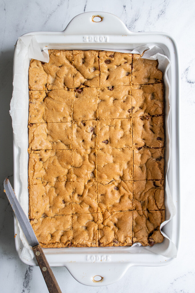 A white baking dish with sliced whole wheat chocolate chip cookie bars and a knife.