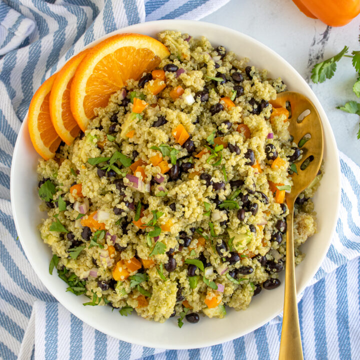 Overhead view of a white bowl filled with black bean quinoa salad garnished with cilantro and orange slices.