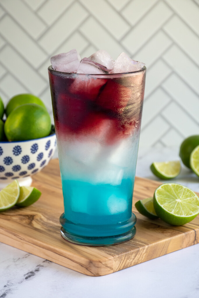 A highball glass filled with ice and layers of red, white, and blue margarita.