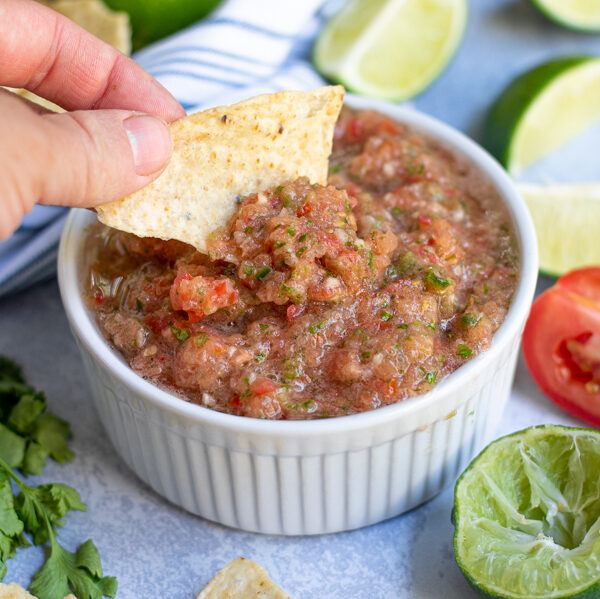 fresh restaurant style salsa being scooped out of a white bowl with a tortilla chip