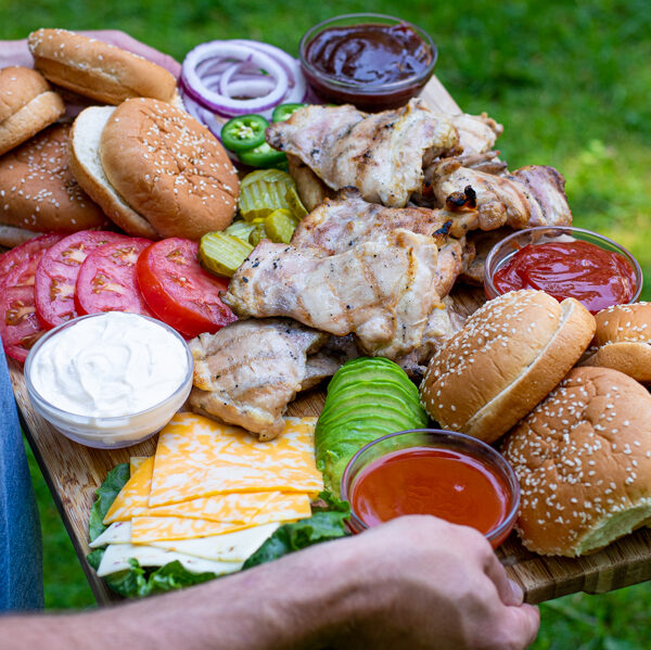 over shoulder shot of a man carrying a large board filled with grilled chicken, buns, and toppings