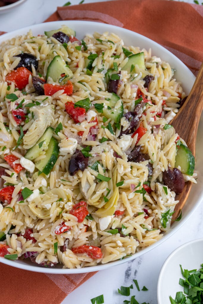 Bowl of Mediterranean Orzo Salad with a wooden spoon.