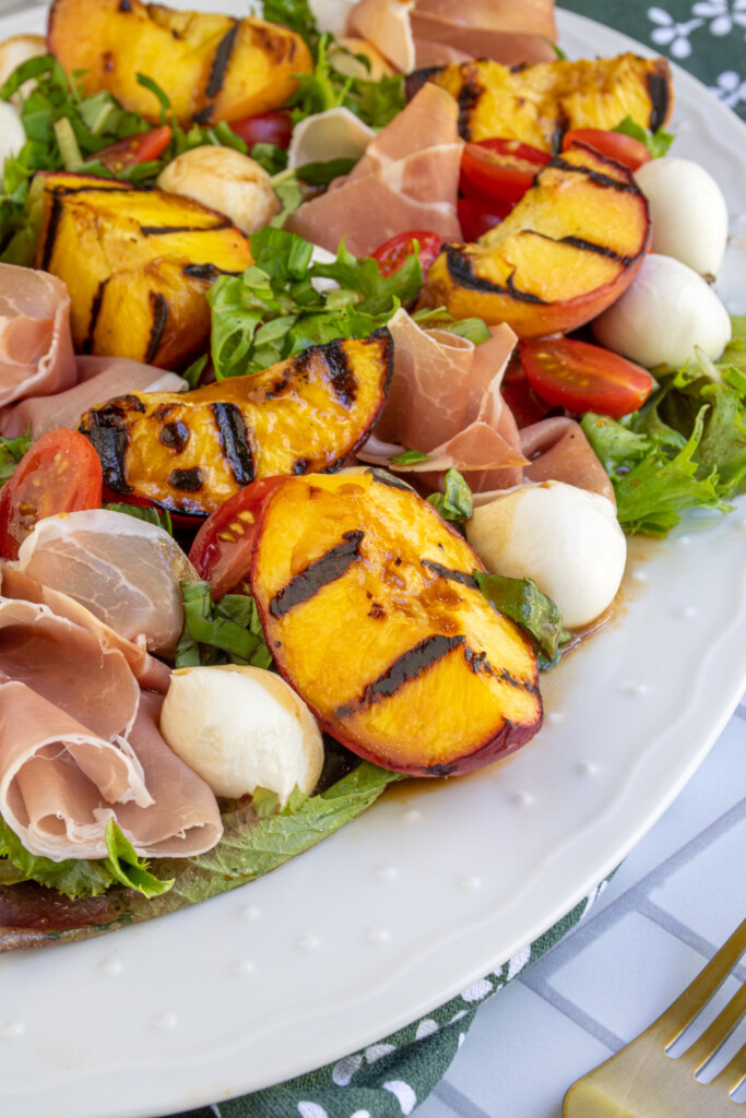 Close up of a grilled peach on a platter of caprese salad.