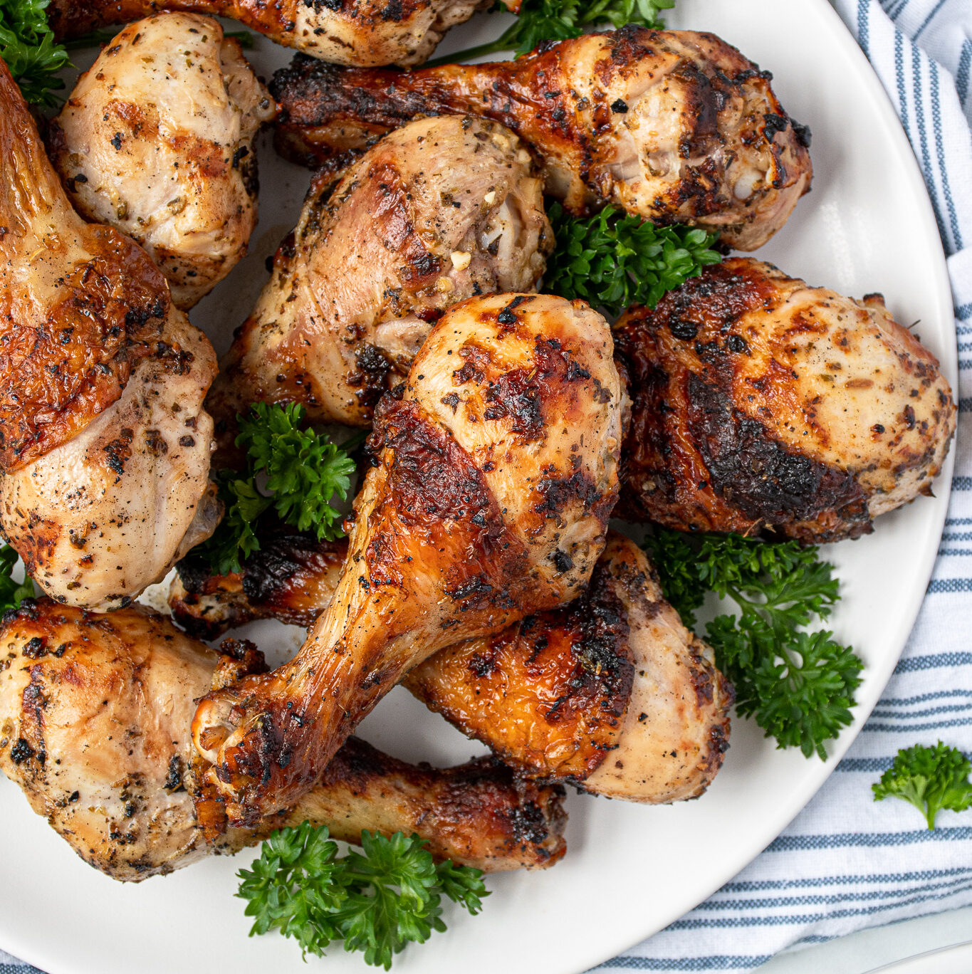 A white plate full of grilled greek marinated chicken drumsticks showing off crispy brown skins.