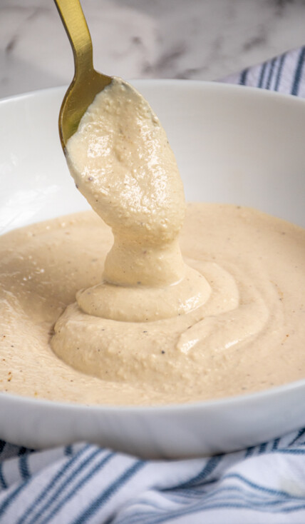 Greek Yogurt Caesar Dressing drizzling off of a spoon into a bowl of dressing.