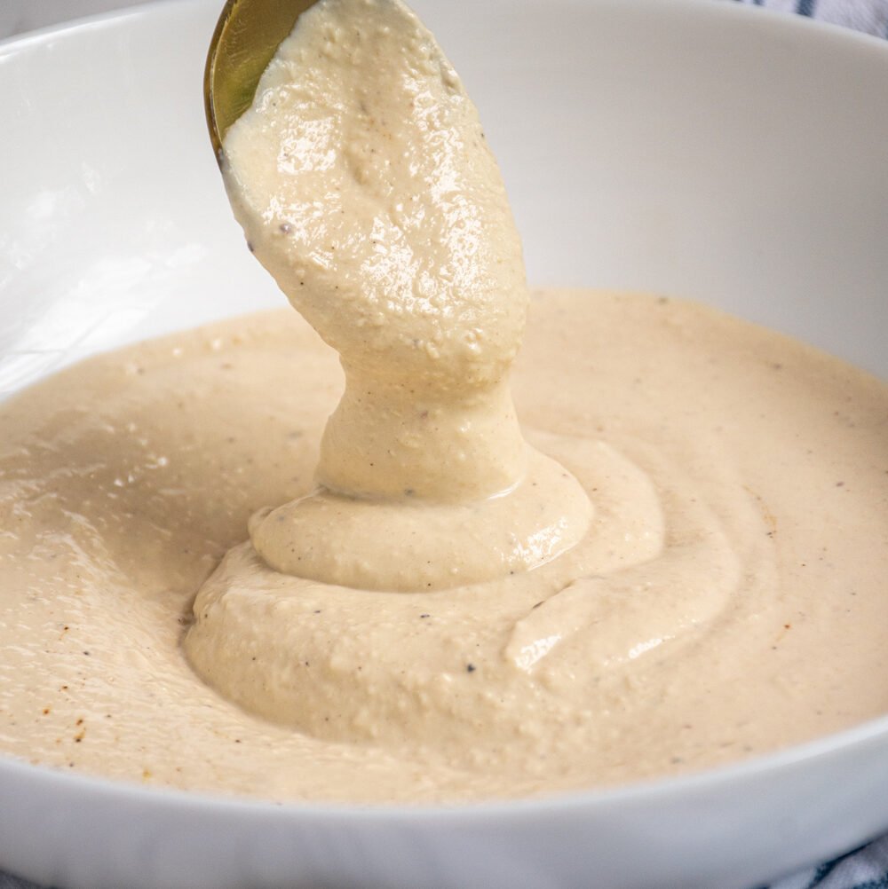 Greek Yogurt Caesar Dressing drizzling off of a spoon into a bowl of dressing.