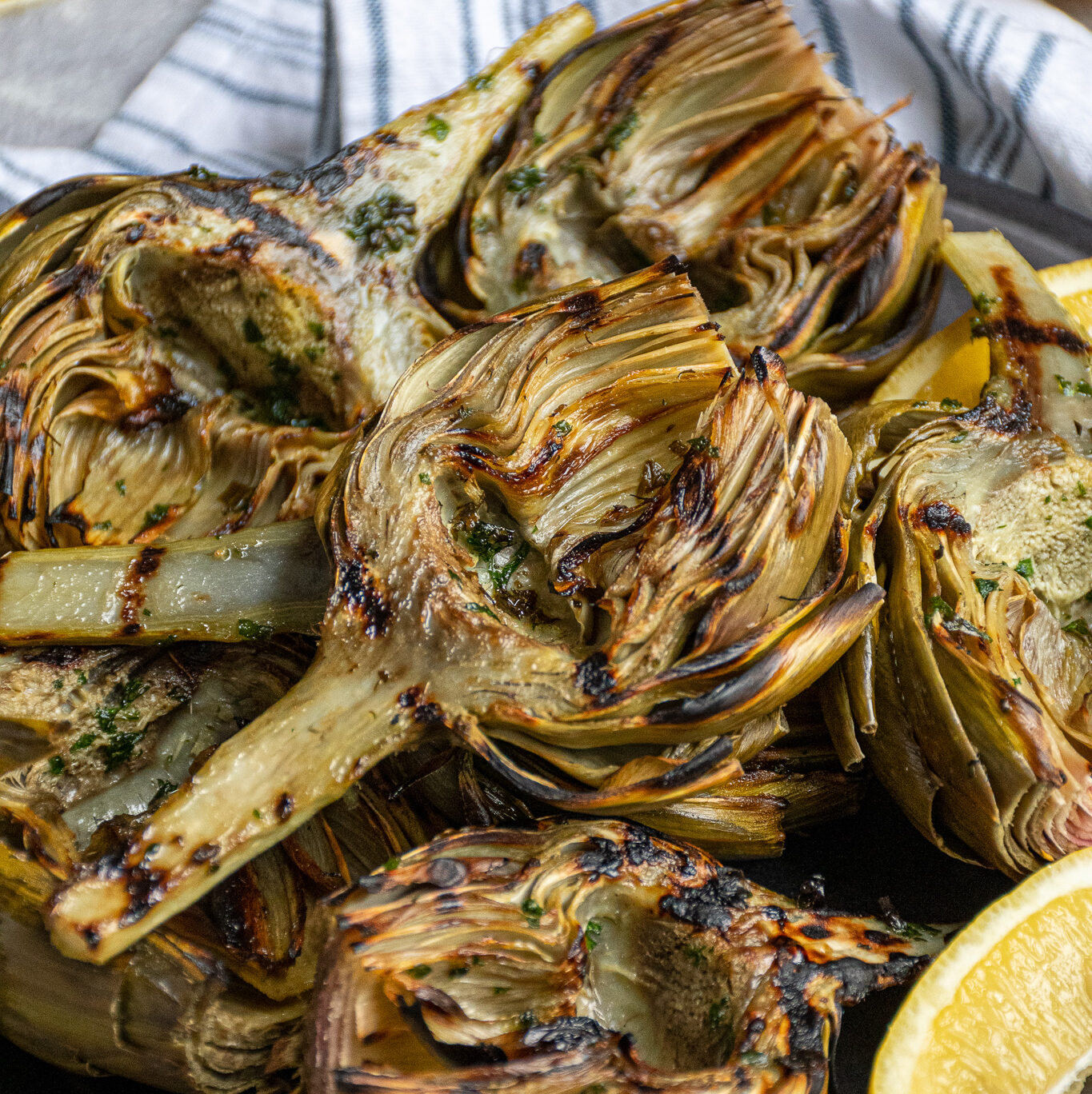 A platter of grilled artichokes with a half of an artichoke on top showing off charred grill marks.