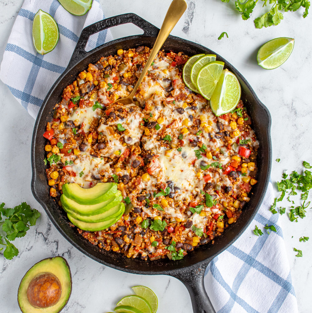 Flatlay of a black cast iron skillet on a table top with colorful corn and peppers topped with cheese and avocado.