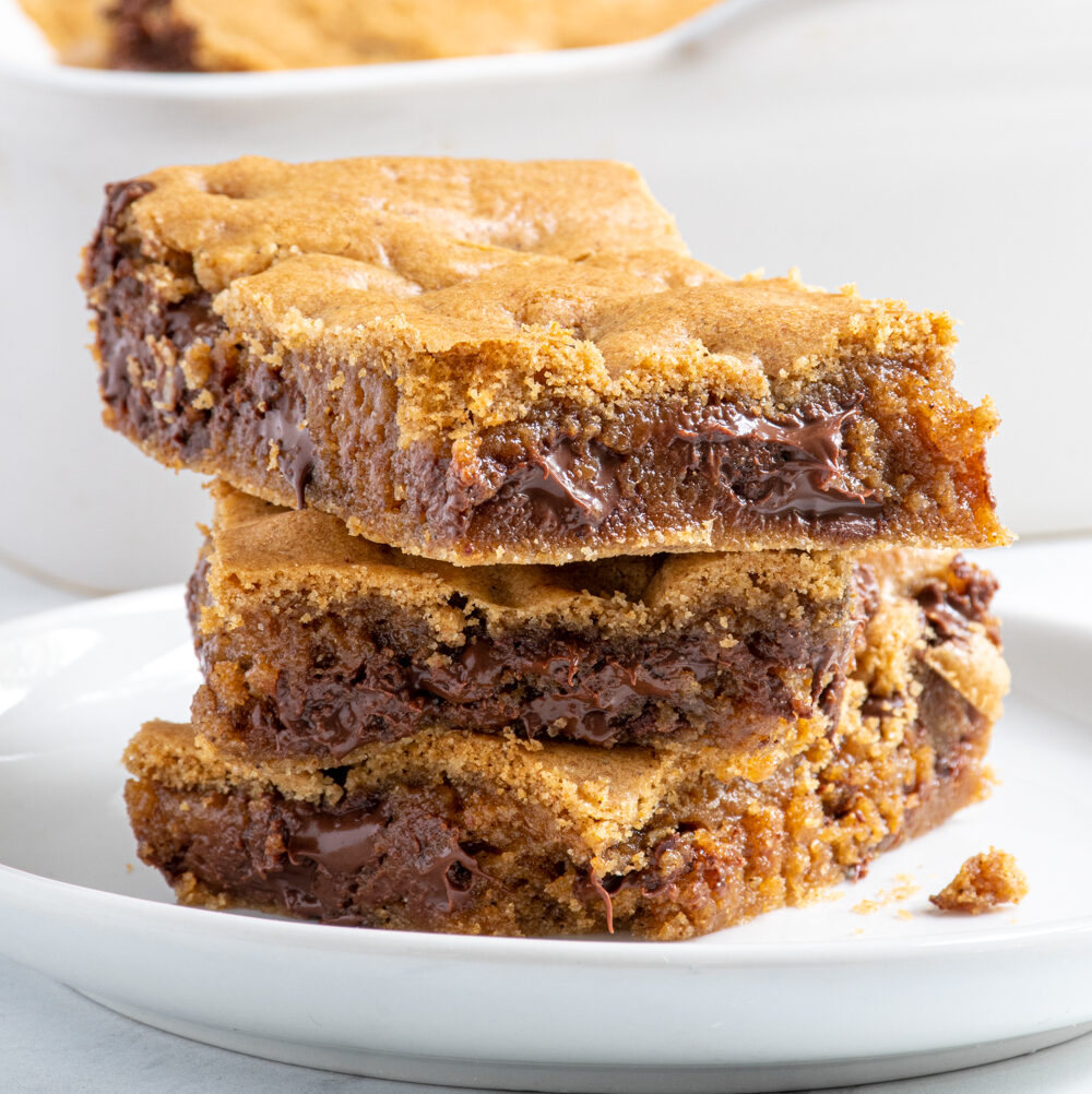 A stack of 3 whole wheat chocolate chip cookie bars on a white plate showing off melty chocolate.