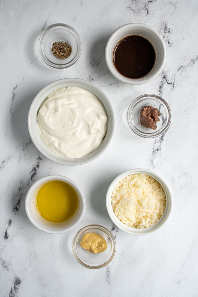 Ingredients for Greek Yogurt Caesar Dressing laid out on a tabletop.