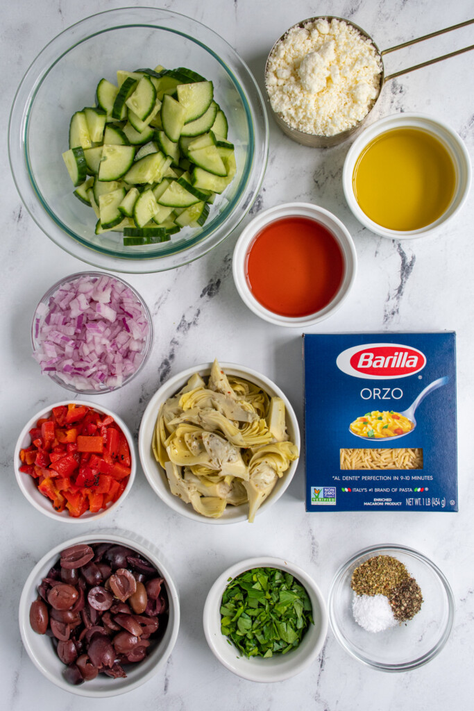 Ingredients needed to make Mediterranean Orzo Pasta Salad all laid out on a table top.
