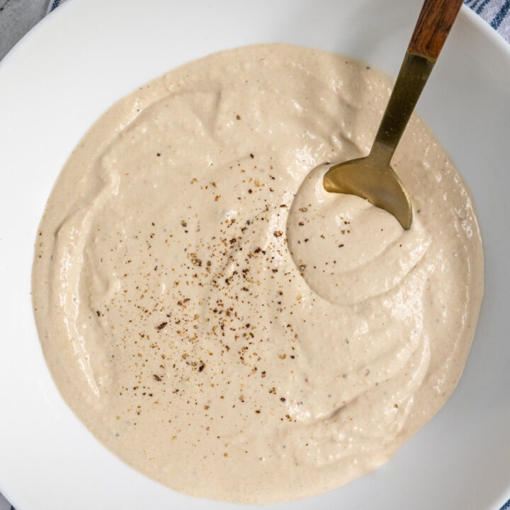 Close up of Greek Yogurt Caesar Dressing in a white bowl topped with freshly ground black pepper.