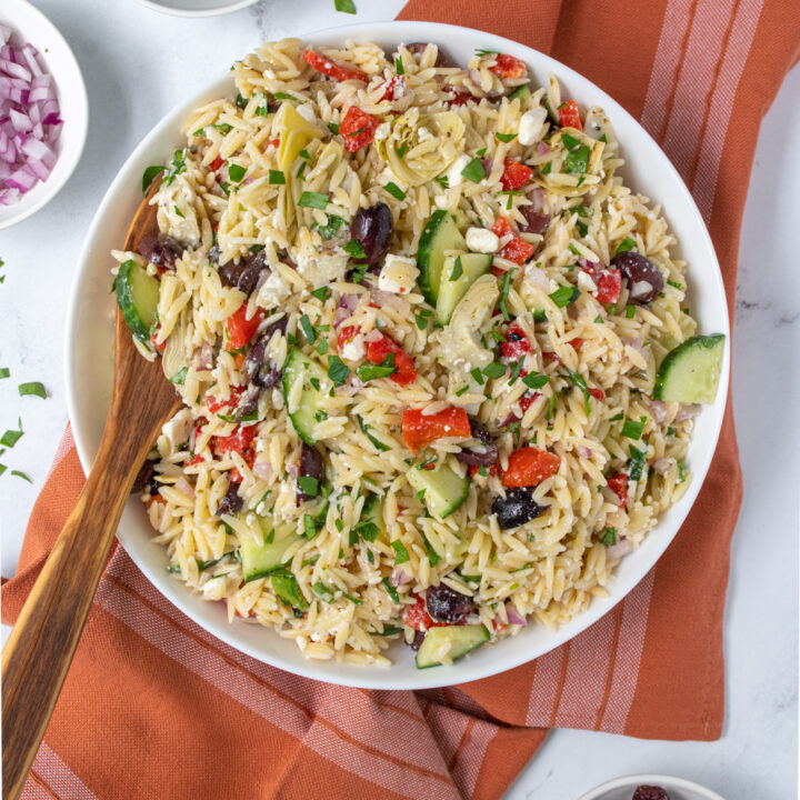 Overhead vouw of a large white bowl filled with Mediterranean Orzo Salad with a wooden spoon and fresh parsley garnish.