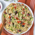 Pinterest Pin with text overlay 'Mediterranean Orzo Pasta Salad', image of a white bowl filled with colorful pasta salad with a wooden spoon.