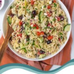 Pinterest Pin with text overlay 'Mediterranean Orzo Pasta Salad', image of a white bowl filled with colorful pasta salad with a wooden spoon.