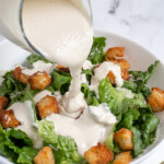 Pinterest pin with text overlay 'Greek Yogurt Caesar Dressing', image of Greek Yogurt Caesar Dressing in a white bowl with a spoon.