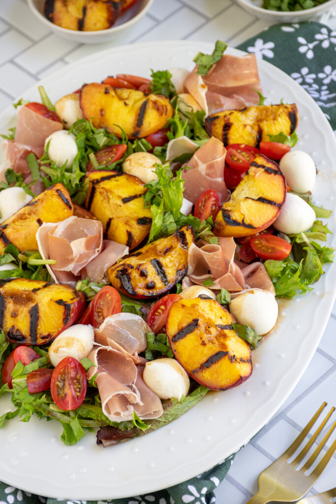 Angled view of a large white platter filled with grilled peach and mozzarella salad.