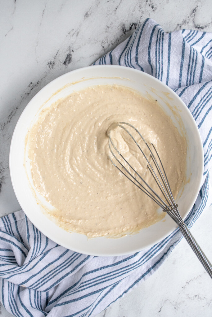 Freshly whisked Greek Yogurt Caesar Dressing on a white bowl.