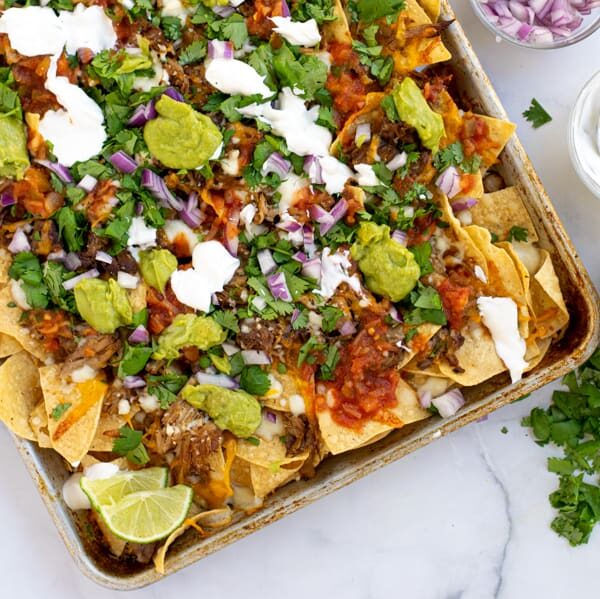 a sheet pan full of carnitas nachos topped with cilantro, red onion, guacamole, and more