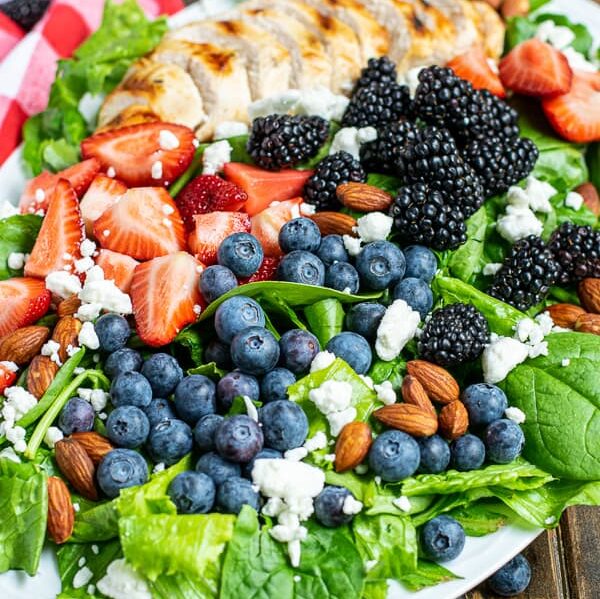 three different kinds of berries with grilled chicken on top of fresh salad greens with almonds and feta cheese on a large platter
