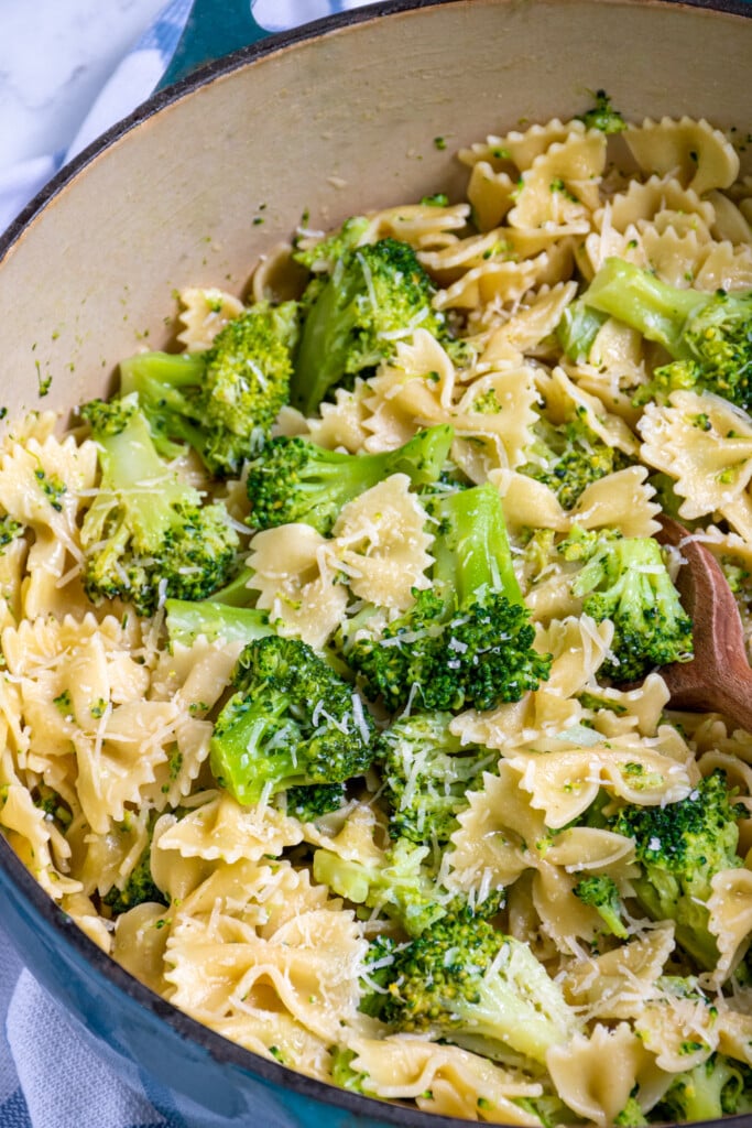 Close up of a large dutch oven filled with green broccoli and bowtie pasta with a wood serving spoon.