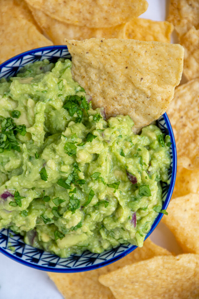 Overhead view of a blue bowl filled with guacamole garnished with cilantro and with a tortilla chip in the bowl.
