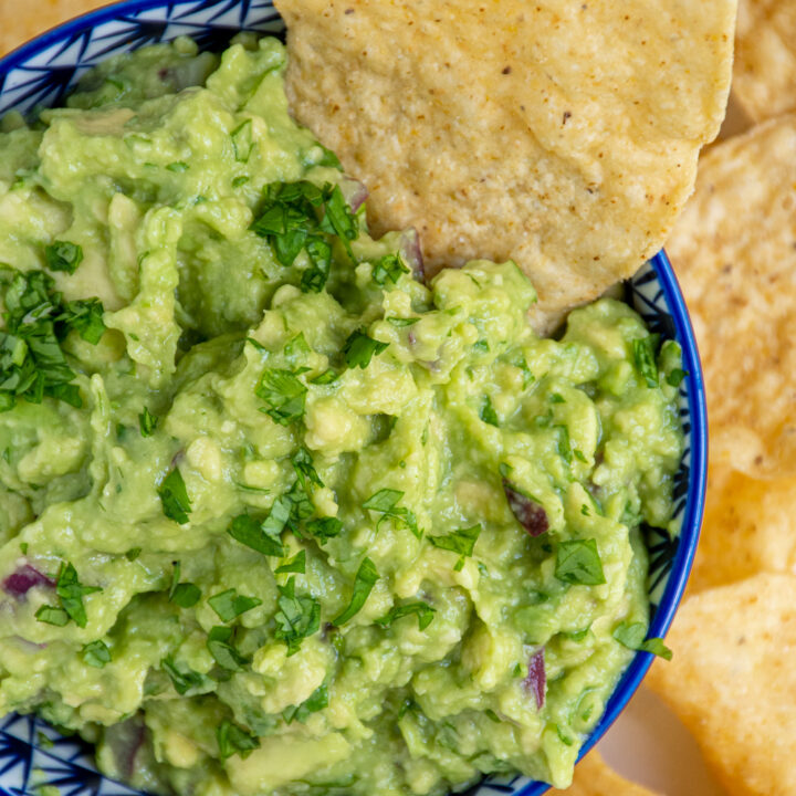 Overhead view of a blue bowl filled with guacamole garnished with cilantro and with a tortilla chip in the bowl.