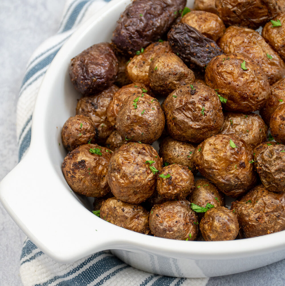 Air fryer baby potatoes in a white ceramic serving dish covered in salt and garnished with chopped parsley.