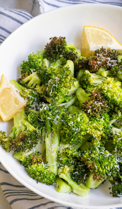A white bowl filled with air fryer broccoli garnished with parmesan cheese and lemon wedges.