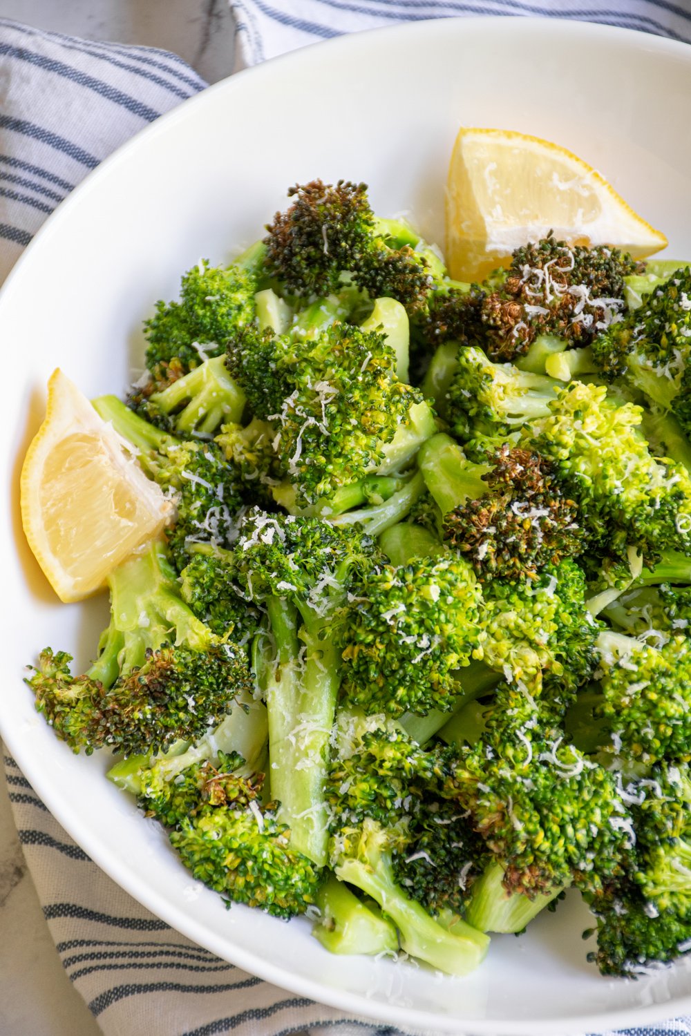 A white bowl filled with air fryer broccoli garnished with parmesan cheese and lemon wedges.