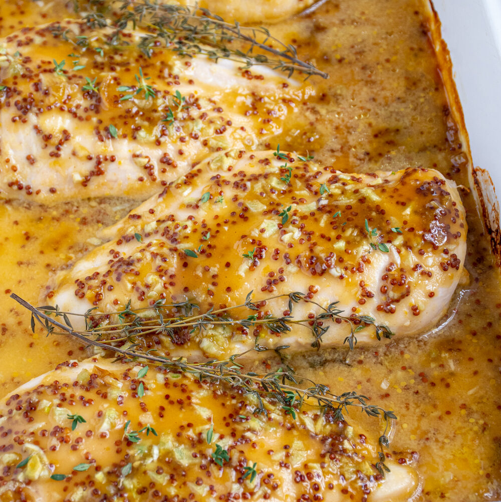 Baked Honey Mustard Chicken in a casserole dish covered in homemade sauce and garnished with fresh thyme.