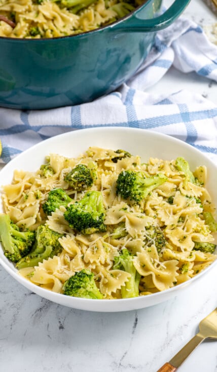 White bowl filled with bowtie pasta and broccoli and garnished with parmesan cheese.