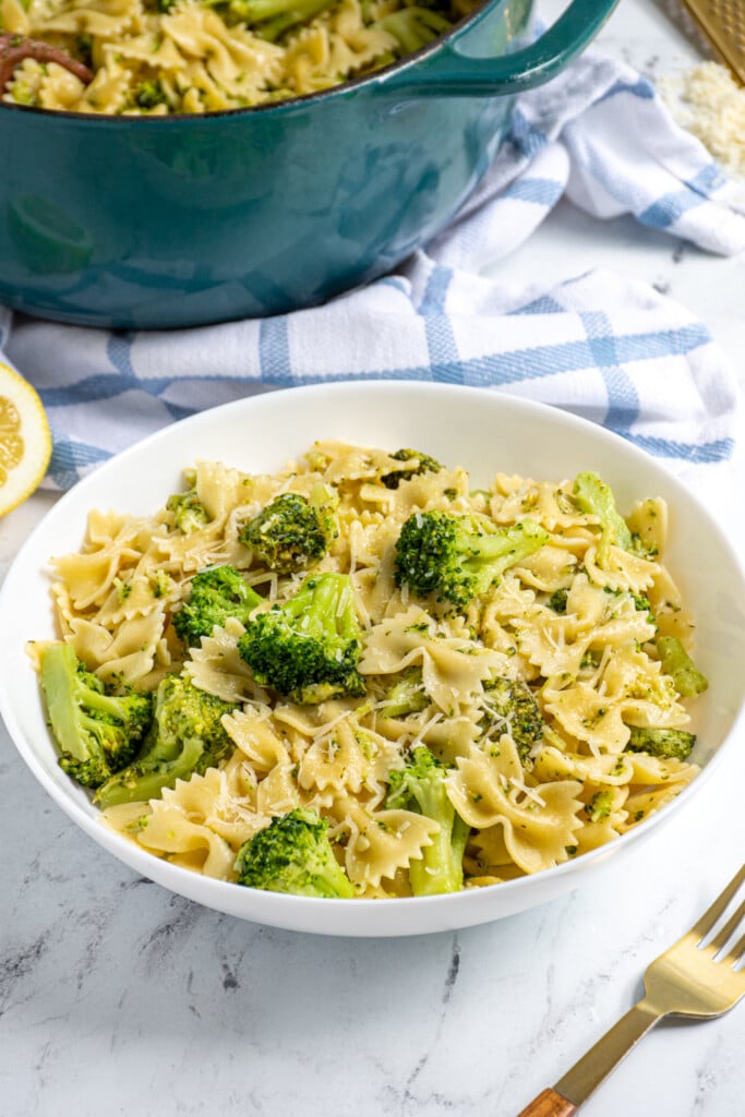 White bowl filled with bowtie pasta and broccoli and garnished with parmesan cheese.