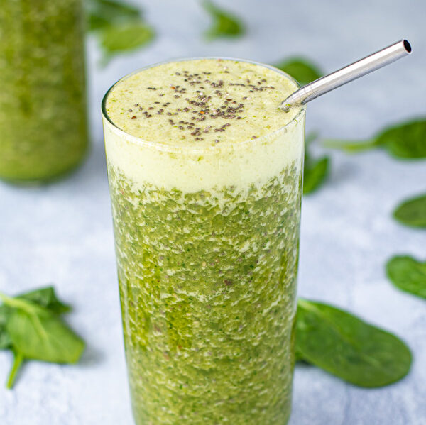 A large glass with a metal straw filled to the top with an energizing green smoothie, topped with chia seeds.