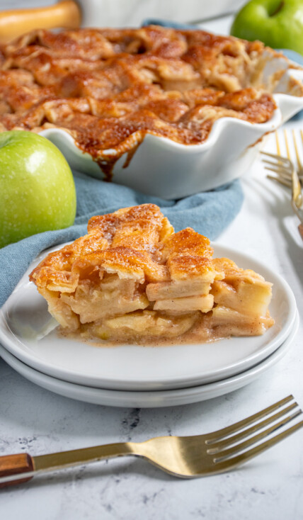 A slice of homemade apple pie on a plate showing of the apple inside and the lattice top.