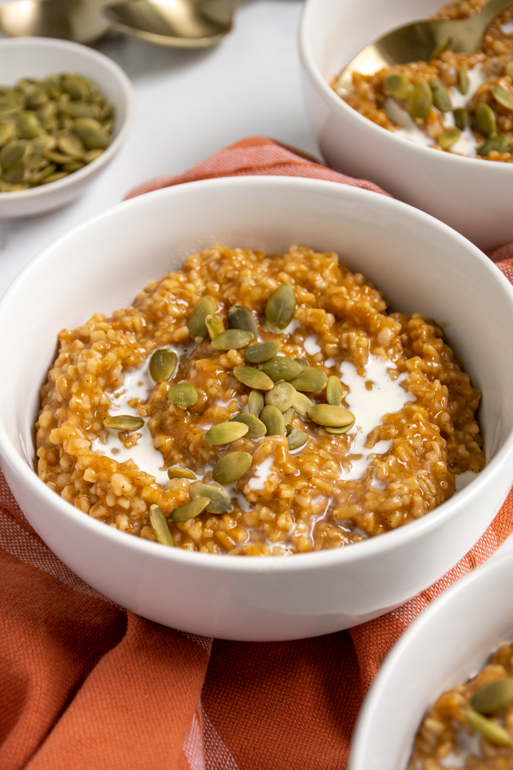 Close up of a white bowl filled with orange hued pumpkin spice steel cut oats that were made in the pressure cooker and topped with cream and pumpkin seeds.