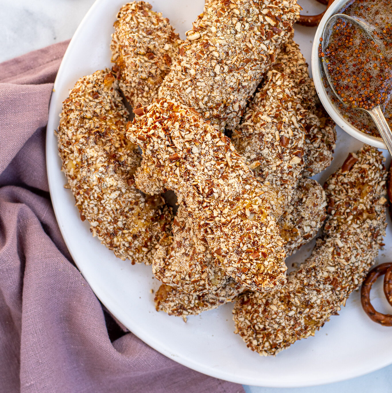 Plate full of a stack of Pretzel Crusted Chicken Tenders next to a small bowl of honey mustard.
