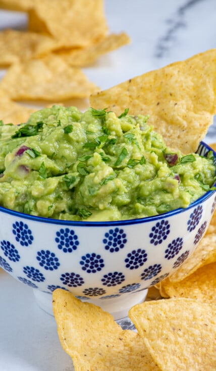 A blue and white bowl filled with simple guacamole and garnished with cilantro and with a tortilla chip.
