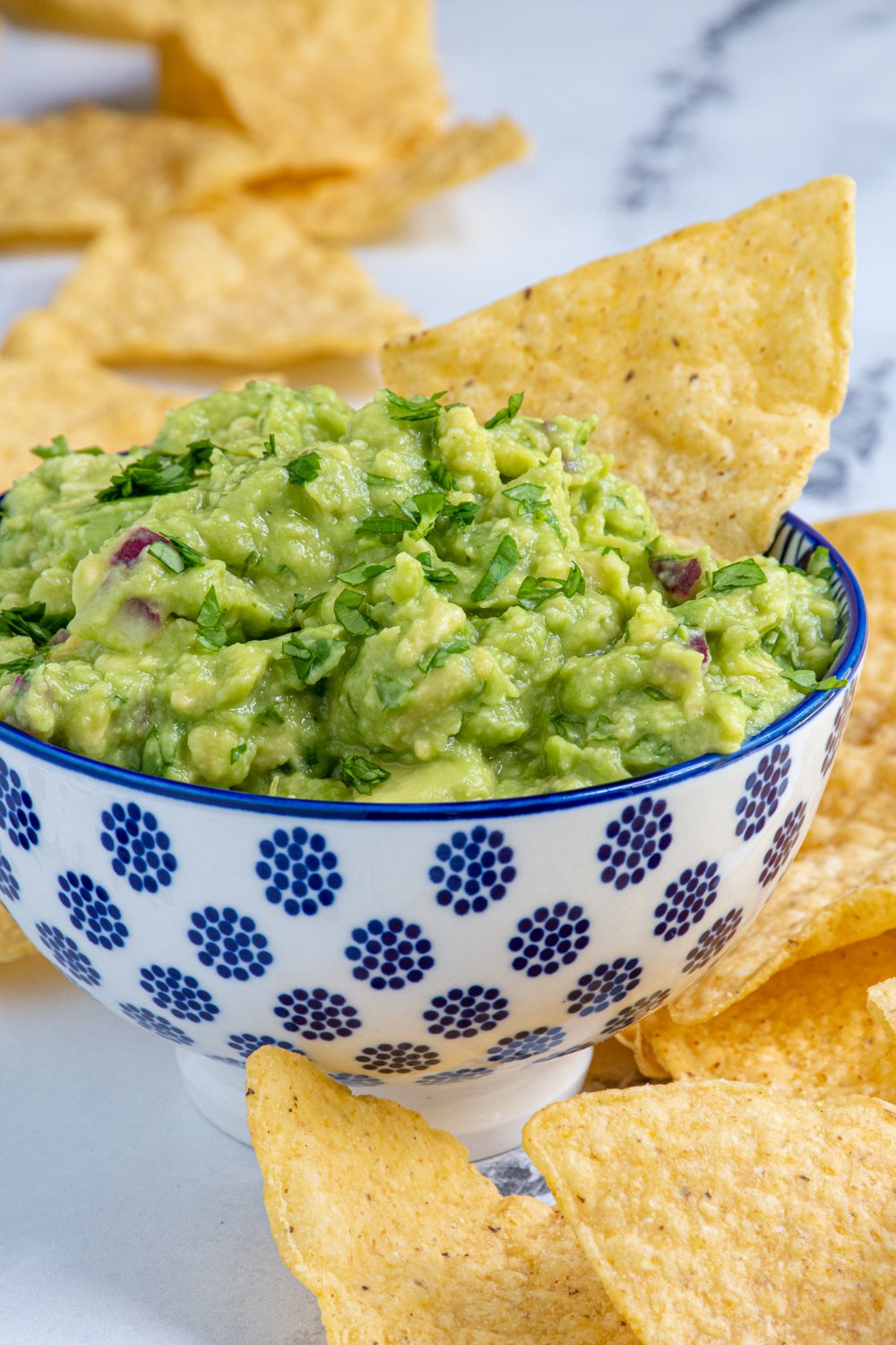 A blue and white bowl filled with simple guacamole and garnished with cilantro and with a tortilla chip.