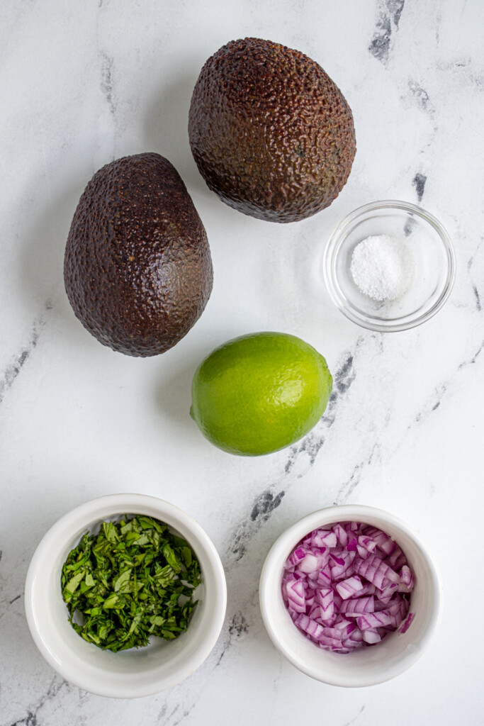 Overhead view of all the ingredients needed to make simple guacamole recipe laid out on a table top.