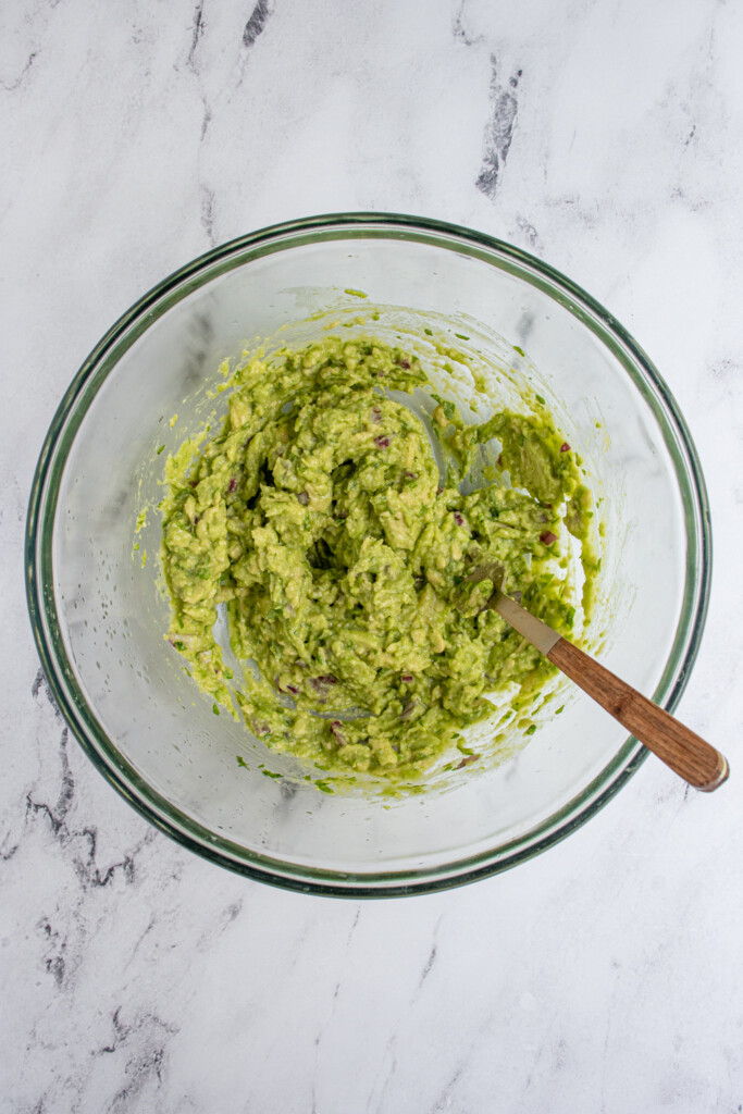 A glass mixing bowl with freshly mixed guacamole and a fork.
