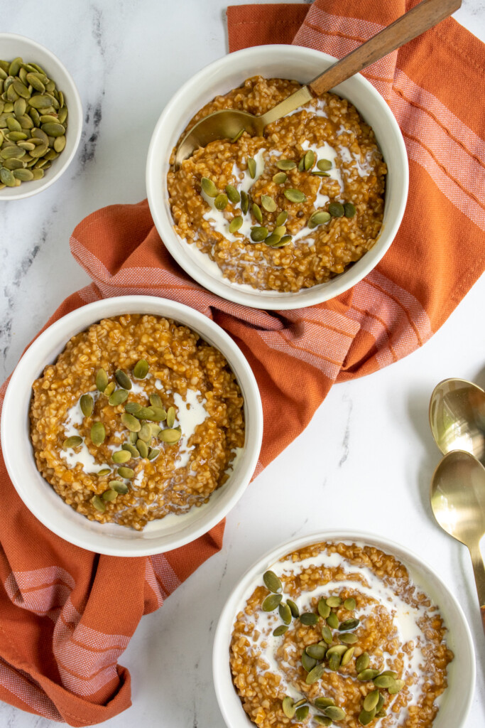 Overhead view of three what bowls on a tabletop filled with pumpkin spice oatmeal.