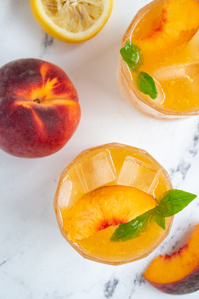 Overhead view of two glasses of Bourbon Peach Smash and a peach.